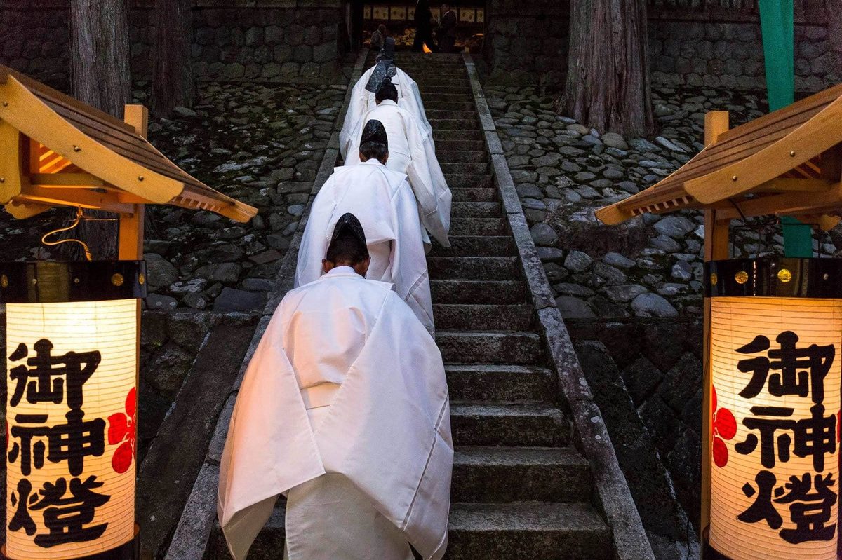 Shrine attendants in white robes climbing the stone steps to Yabuhara Shrine at dusk